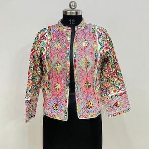 May include: A colorful, embroidered jacket with a mandarin collar. The jacket features intricate patterns in red, green, blue, and yellow, with small mirrors incorporated into the design. The jacket is displayed on a mannequin.