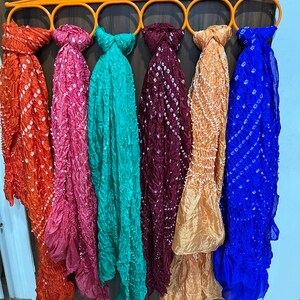 Peut inclure: Six foulards color&eacute;s suspendus &agrave; un cintre orange circulaire. Les foulards sont faits d'un tissu doux et transparent avec un motif tie-dye. Les couleurs des foulards sont orange, rose, turquoise, marron, or et bleu.