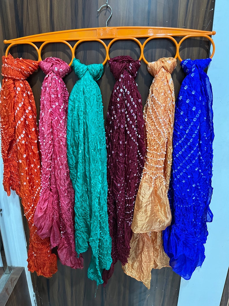 Peut inclure: Six foulards color&eacute;s suspendus &agrave; un cintre orange circulaire. Les foulards sont faits d'un tissu doux et transparent avec un motif tie-dye. Les couleurs des foulards sont orange, rose, turquoise, marron, or et bleu.