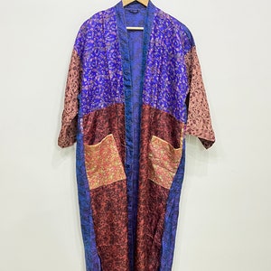 May include: A long, patchwork robe with a floral pattern in shades of blue, burgundy, and pink. The robe has two pockets and is hanging on a wooden hanger. The robe is made of a silky material.