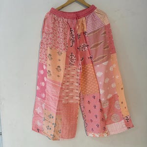 Könnte beinhalten: Weit geschnittene Hose mit Patchwork-Design in verschiedenen Rosa-, Pfirsich- und Weißtönen. Das Kleidungsstück verfügt über einen elastischen Bund mit Kordelzug und besteht aus mehreren Stoffbahnen, die jeweils unterschiedliche Blumen- und Geometriemuster zeigen.