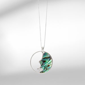 May include: A silver chain necklace with a circular pendant featuring a half-circle of abalone shell with green, blue, and black iridescent colors.