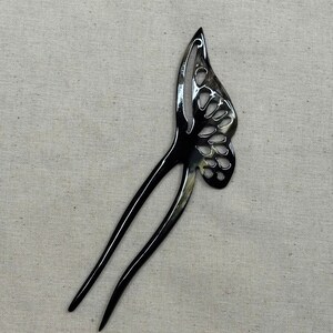 May include: A black butterfly-shaped hair fork with a glossy finish. The butterfly wing design features cut-out details. The hair accessory has two long, slender prongs extending from the wing.