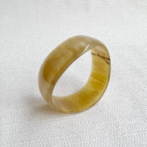 Pu&ograve; includere: Un bracciale rigido traslucido color miele con una superficie liscia e lucida. L'accessorio circolare presenta sottili motivi vorticosi in tonalit&agrave; ambra chiare e scure su tutta la sua fascia spessa e arrotondata.
