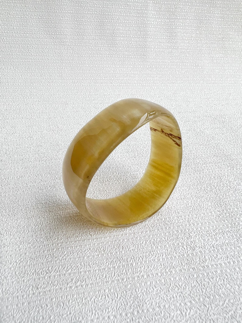 Pu&ograve; includere: Un bracciale rigido traslucido color miele con una superficie liscia e lucida. L'accessorio circolare presenta sottili motivi vorticosi in tonalit&agrave; ambra chiare e scure su tutta la sua fascia spessa e arrotondata.