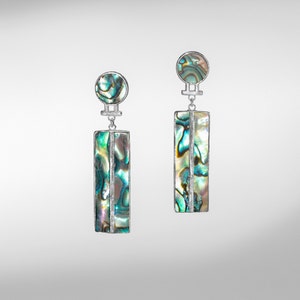May include: A pair of silver dangle earrings with iridescent abalone shell accents. The earrings feature a rectangular shape with a silver bar running down the center.