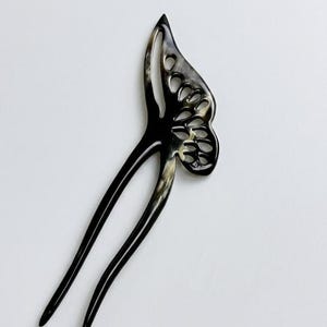 May include: A black and cream-colored hair fork with a butterfly wing design. The hair accessory has a glossy finish and a forked base. The butterfly wing features cut-out details.