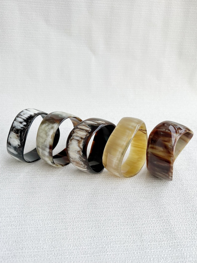 Pu&ograve; includere: Cinque bracciali rigidi lisci e lucidi disposti in fila. Ogni bracciale presenta un motivo naturale unico con varie tonalit&agrave; di nero, bianco, grigio, marrone chiaro e marrone scuro, con una finitura lucida e semitrasparente.