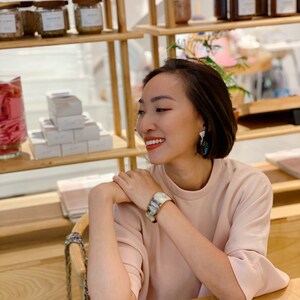 Pu&ograve; includere: Un top a maniche corte rosa chiaro indossato con un ampio bracciale a polsino con motivo marmorizzato nei toni del marrone, bianco e grigio, e orecchini pendenti con un design geometrico scuro e multicolore con una parte superiore in metallo argentato.