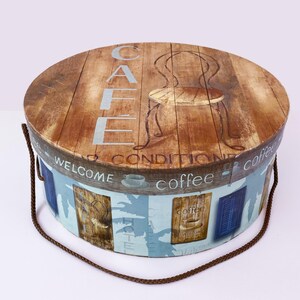 May include: A round, wooden storage box with a blue and white design. The top of the box features a woodgrain pattern with the word "CAFE" written vertically and a chair illustration. The bottom of the box has a blue and white design with the words "Welcome", "Conditioned", and "Coffee" written around the box.