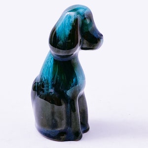 May include: A small ceramic dog figurine in a sitting position. The dog is glazed in shades of blue and green, with a black base.