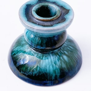 May include: A blue and green ceramic candle holder with a swirl pattern. The holder has a wide base and a narrow top.