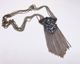 May include: A silver chain necklace with a large, ornate pendant featuring a geometric design and blue stones.