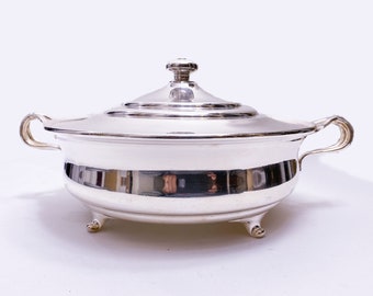 May include: A silver serving dish with a lid and two handles. The dish has a round shape and sits on four small feet.