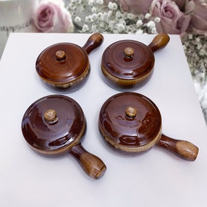 May include: Four brown ceramic ramekins with lids and handles. The ramekins are glazed in a brown and cream colour.