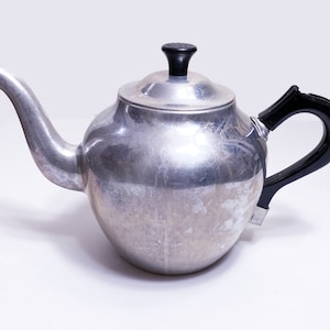 May include: A silver aluminum teapot with a black plastic handle and lid.