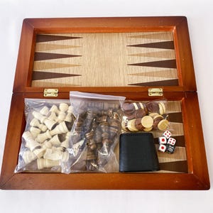 Könnte beinhalten: Ein Backgammon-Spiel aus Holz mit einem braunen und beigefarbenen Brett, weißen und braunen Spielsteinen, Würfeln und einem schwarzen Beutel. Das Set ist geöffnet und die Spielsteine sind sichtbar.
