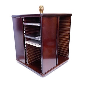 May include: A dark brown wooden CD storage tower with a gold finial on top. The tower has multiple shelves for storing CDs and is in a closed position.