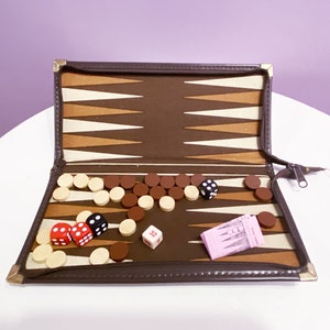 May include: A brown leather backgammon game set with a brown and beige playing board, white and brown playing pieces, and red and black dice. The game is open and ready to play.