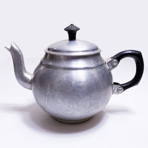 May include: A silver teapot with a black plastic handle and a black knob on the lid.