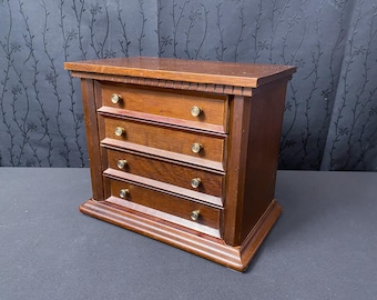 May include: A dark wood chest of drawers with five drawers and brass knobs. The chest is on a black background.
