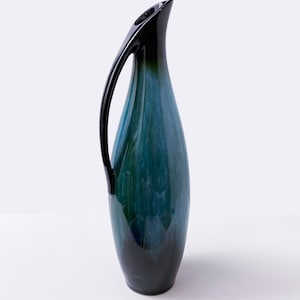 May include: A blue and black ceramic vase with a curved handle. The vase has a glossy finish and a unique, abstract design.