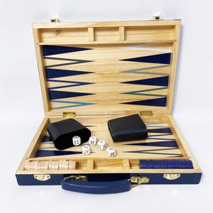 May include: Open wooden backgammon set with a navy blue exterior and interior design. The game board features a light wood grain with navy blue, teal, and grey triangles. Includes black dice cups, dice, and game pieces.