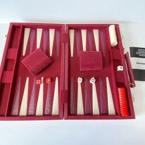 Könnte beinhalten: Offenes Backgammon-Set mit bordeauxrotem Samtinterieur und elfenbein- und burgunderfarbenen Spielpunkten. Enthält Würfel, einen Verdopplungswürfel und ein Büchlein. Das Set befindet sich in offener Position und ist spielbereit.