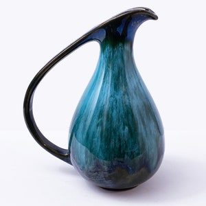 Peut inclure: Un pichet en céramique bleu sarcelle avec une anse noire et un bec unique et incurvé. Le pichet a une finition brillante et un glaçage marbré.