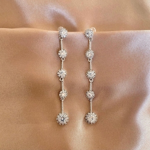 Può includere: Un paio di orecchini pendenti in argento con cinque pietre di cristallo trasparenti su ogni orecchino.