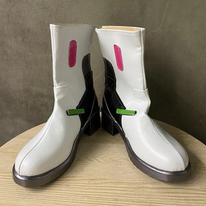 Könnte beinhalten: Weiße Stiefel mit mittelhohem Schaft, schwarzen Akzenten und Blockabsatz. Die Stiefel haben ein rosa Rechteckdetail und einen grünen Riemen. Die Sohlen sind dunkelgrau. Die Höhe beträgt ca. 20 cm.