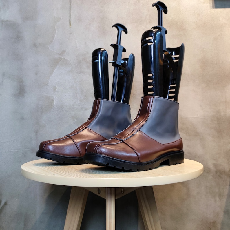 May include: A pair of brown leather boots with gray fabric panels and black boot shapers. The boots are sitting on a light wood table.