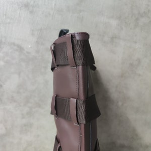 May include: A brown leather bag with adjustable straps and a buckle closure. The bag has a textured surface and a simple design.