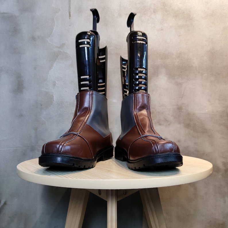 May include: A pair of brown leather boots with black shoe trees inside. The boots are sitting on a light brown wooden table.