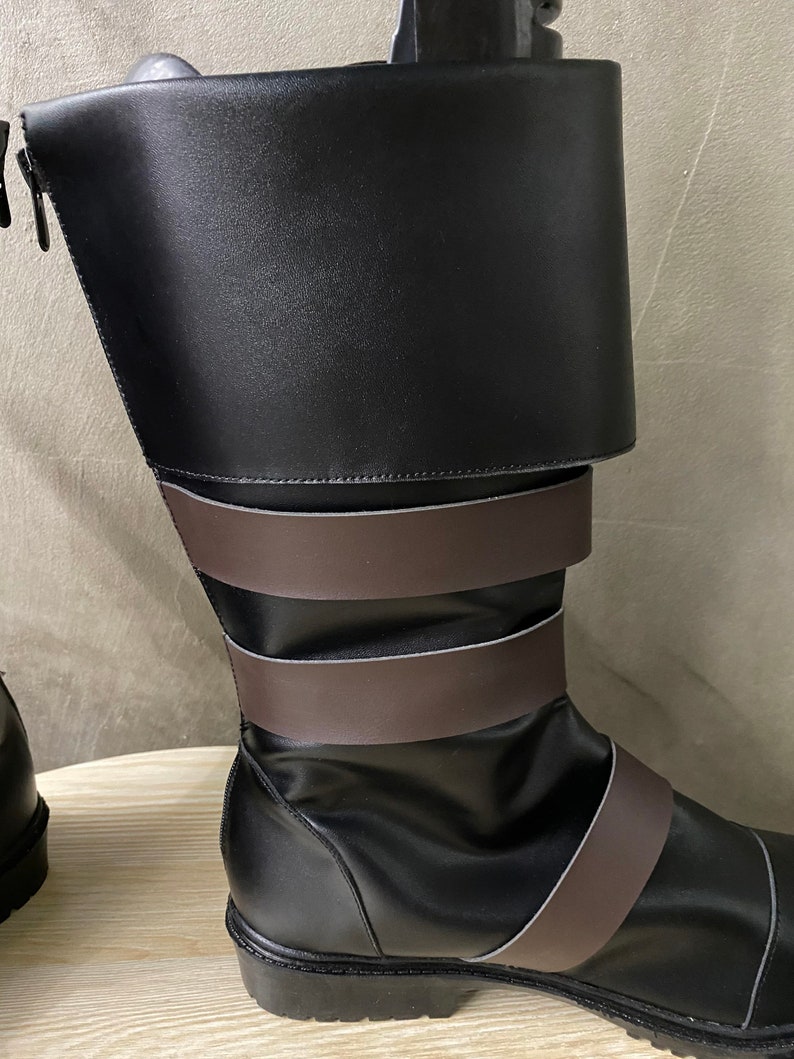 K&ouml;nnte beinhalten: Schwarze Lederstiefel mit braunen Riemen. Die Stiefel haben einen Rei&szlig;verschluss an der Seite und einen umklappbaren Schaft.