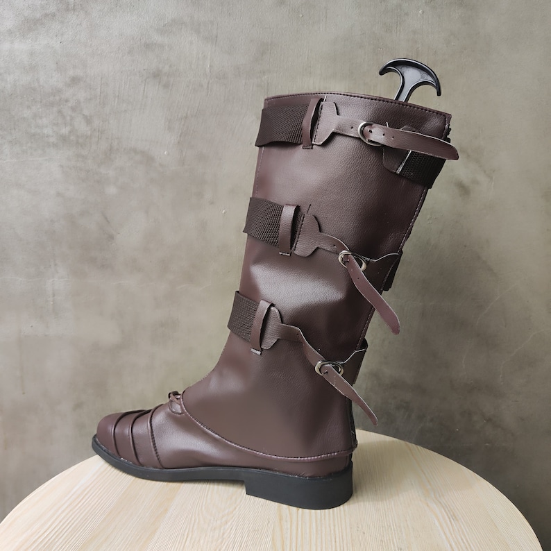 May include: Brown leather knee-high boots with multiple buckles and straps. The boots have a pointed toe and a low heel.