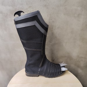 May include: Black and gray knee-high boots with a pointed toe and a textured fabric upper. The boots have a zipper on the inside of the leg and a decorative strap across the top of the foot.