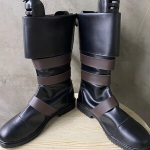 K&ouml;nnte beinhalten: Ein Paar schwarze Lederstiefel mit braunen Lederriemen. Die Stiefel haben eine abgerundete Spitze und eine dicke Sohle.