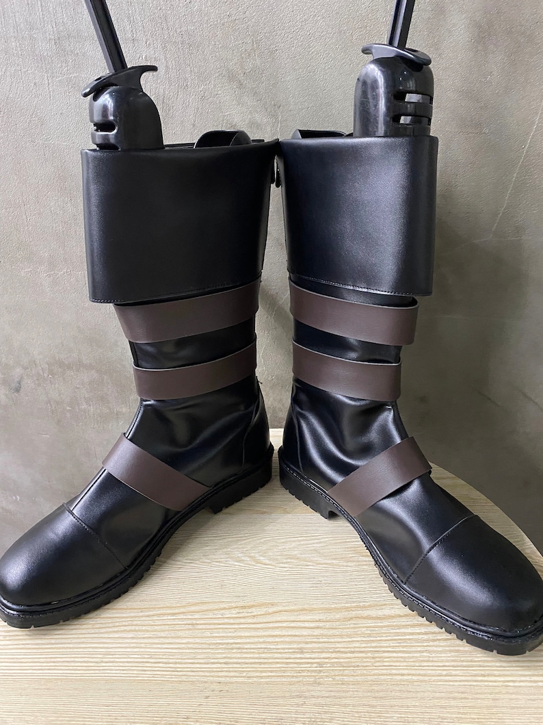 K&ouml;nnte beinhalten: Ein Paar schwarze Lederstiefel mit braunen Lederriemen. Die Stiefel haben eine abgerundete Spitze und eine dicke Sohle.