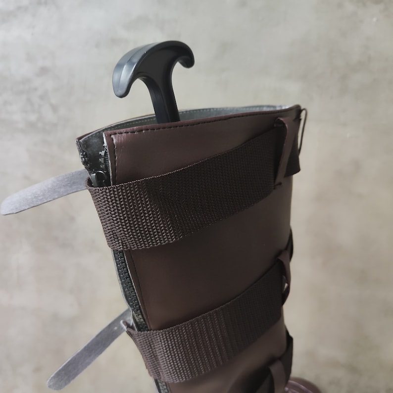 May include: Close-up of the top of a brown leather boot with multiple adjustable straps and a black plastic boot puller.