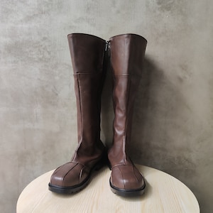 Puede incluir: Un par de botas de cuero marrón de caña alta con cremallera en la parte posterior de cada bota.