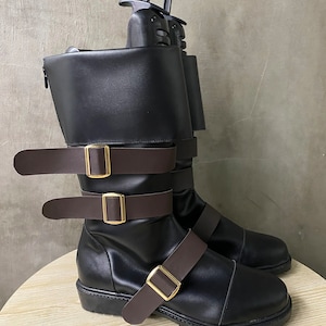 K&ouml;nnte beinhalten: Schwarze Lederstiefel mit braunen Riemen und goldenen Schnallen. Die Stiefel haben einen Rei&szlig;verschluss an der Seite und eine dicke Sohle.