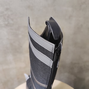 May include: A black tall boot with a zipper on the side. The boot has a gray reflective stripe on the back.