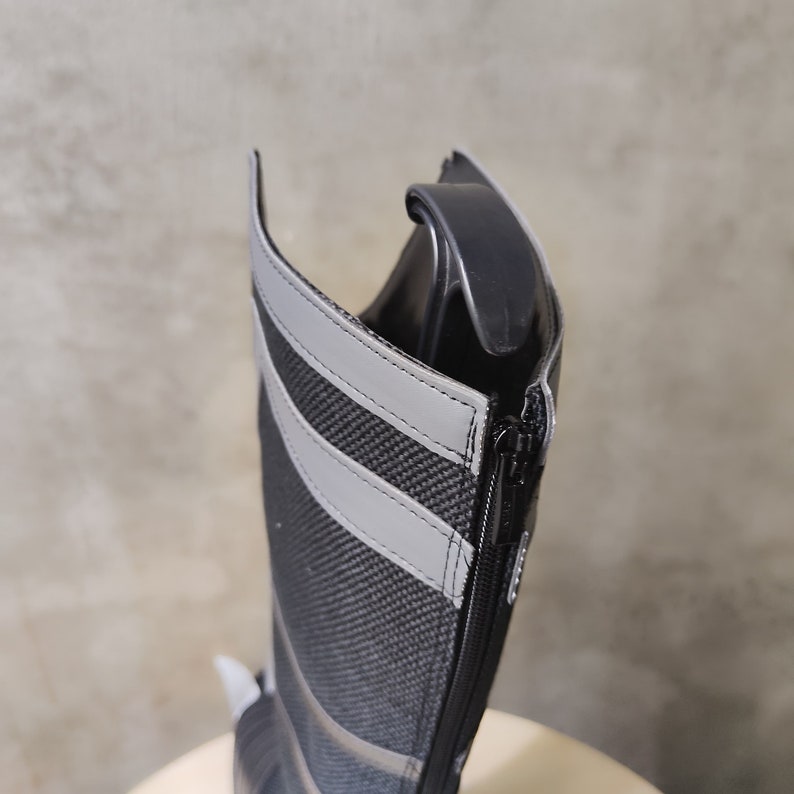 May include: A black tall boot with a zipper on the side. The boot has a gray reflective stripe on the back.