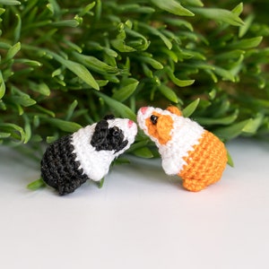 Pode incluir: Dois brinquedos de cobaia de croch&ecirc;, um preto e branco e outro laranja e branco, que se olham.