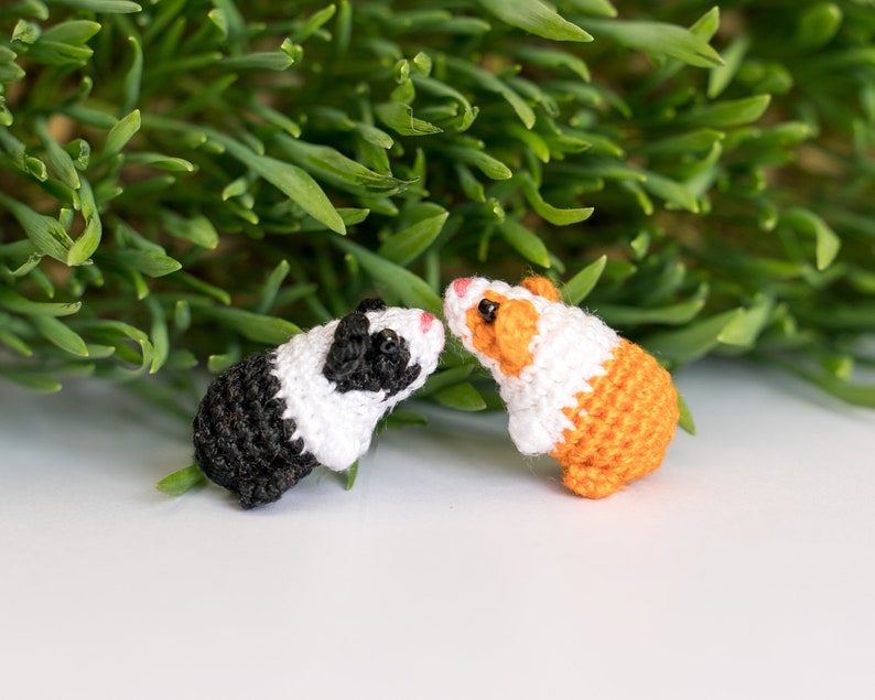 Pode incluir: Dois brinquedos de cobaia de croch&ecirc;, um preto e branco e outro laranja e branco, que se olham.