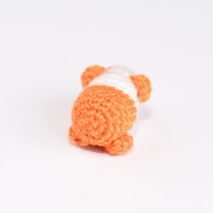 Pode incluir: Um pequeno brinquedo de croch&ecirc; em forma de porco. O porco &eacute; laranja e branco com a barriga branca e as orelhas e as patas laranja.