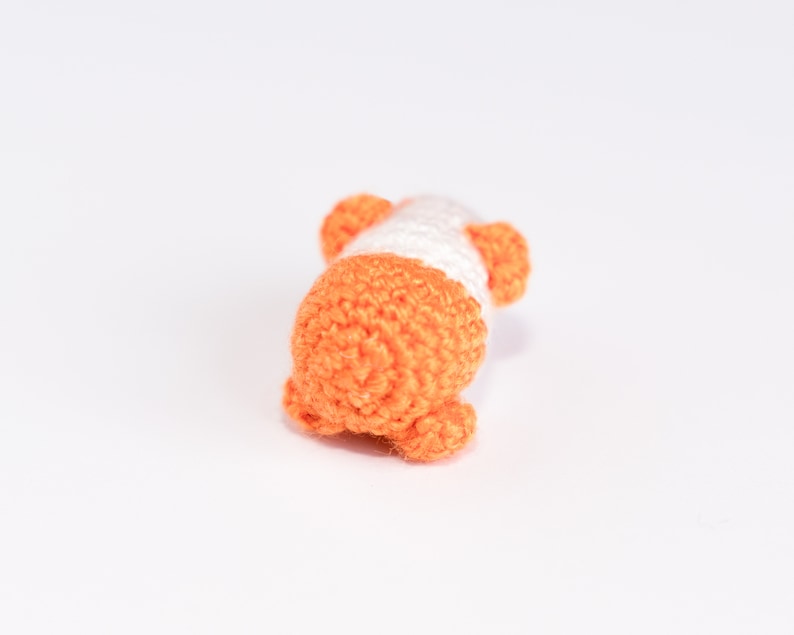 Pode incluir: Um pequeno brinquedo de croch&ecirc; em forma de porco. O porco &eacute; laranja e branco com a barriga branca e as orelhas e as patas laranja.