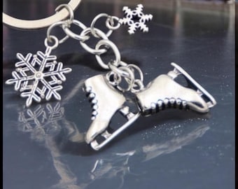 May include: Silver-toned keychain featuring a pair of ice skates and two snowflake charms. The skates are detailed with laces and blades. The keychain is attached to a silver ring.