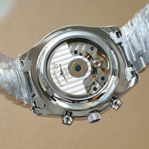 Op de afbeelding: Close-up van een zilverkleurig polshorloge met een transparante achterkant, waardoor de ingewikkelde interne werking van het horloge zichtbaar is. Het horloge heeft een zilveren band en een ronde wijzerplaat met de merknaam "Longines".